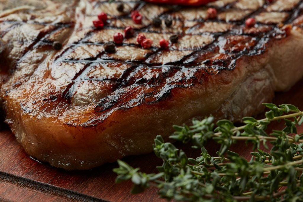 Close-up of succulent grilled ribeye steak with peppercorn and fresh thyme on a wooden board.